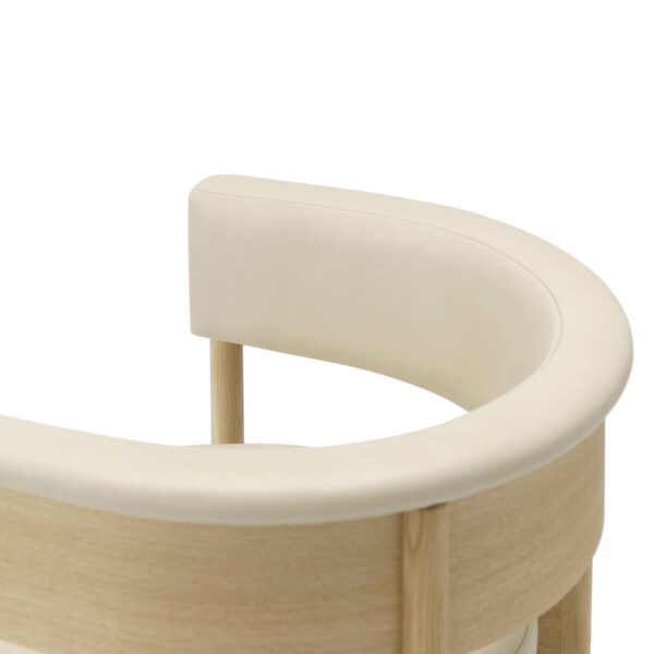 a close-up view of the backrest of a Circa Dining Armchair. The backrest is upholstered in a smooth, cream-colored fabric and is curved to provide comfortable support. The frame is made from light-toned wood, which complements the upholstery. The close-up angle highlights the chair's elegant and minimalist design, focusing on the seamless joinery and high-quality materials used.