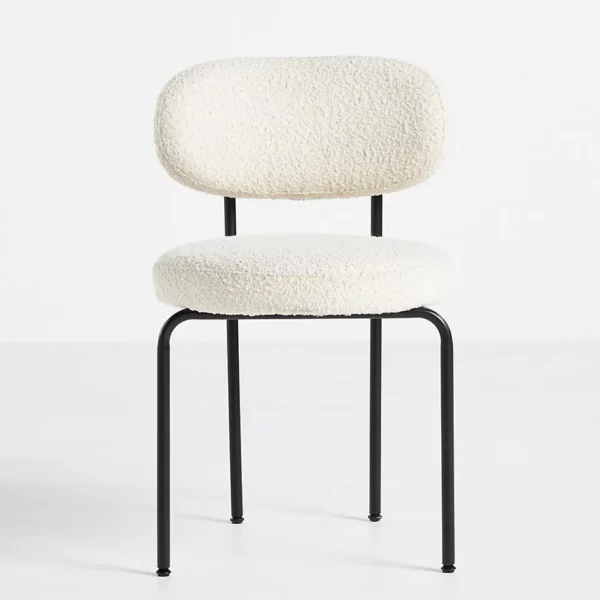 A modern dining chair featuring a plush, white boucle upholstered seat and backrest. The chair has a minimalist design with black metal legs that provide a sleek and sturdy support. The rounded edges of the seat and backrest add a touch of softness to the overall aesthetic.