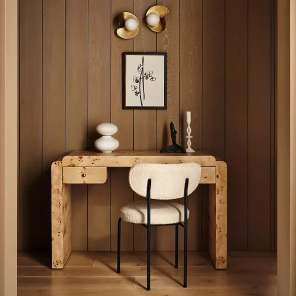 Cozy home office with a wooden desk and a white boucle chair with black metal legs, set against a wooden paneled wall.