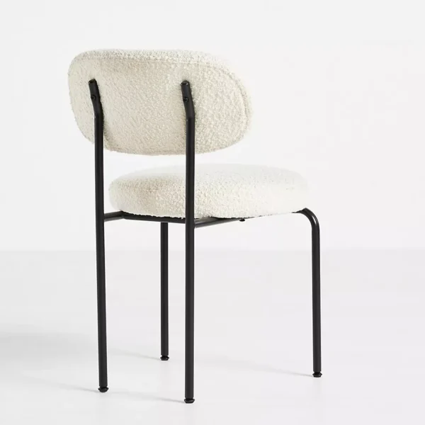 Rear view of a modern dining chair with white boucle upholstery and black metal legs.