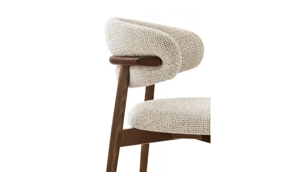 Side view of Caelina Wooden Dining Chair with curved, upholstered backrest and seat in light textured fabric.
