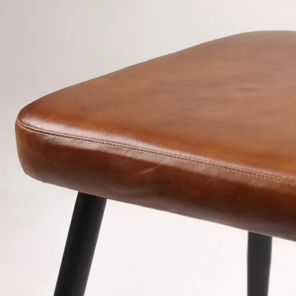 Close-up of the cushioned brown leather seat of a modern dining chair, highlighting the fine stitching and smooth texture, supported by black metal legs