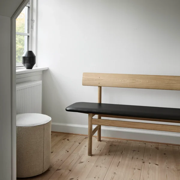 Visiteur oak wood bench with black faux leather seat positioned by the window, featuring minimalist Scandinavian design and natural wood aesthetics