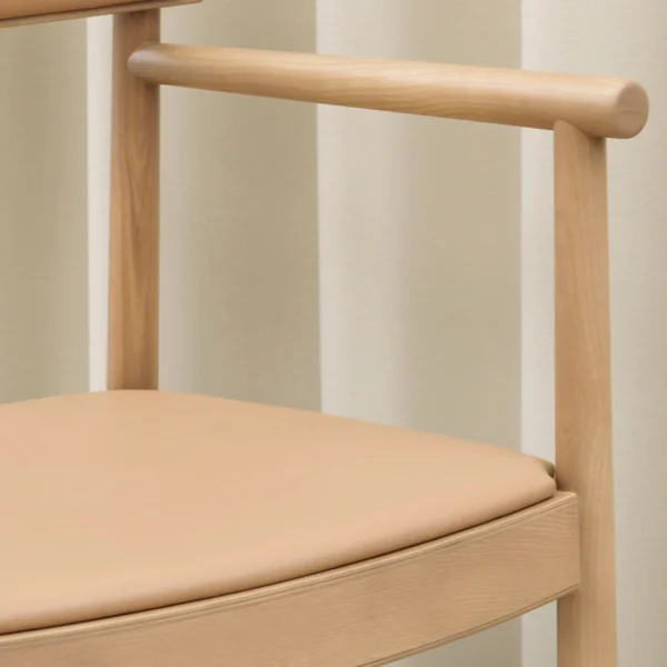 Side view of a wooden chair with a light natural wood frame and beige upholstered seat, featuring minimalist design