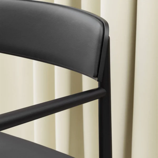 Close-up of the backrest and armrest of tobi black dining armchair with a wooden frame, highlighting the sleek and modern design