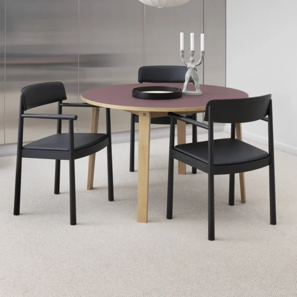 Modern dining room setup featuring a round table with a wooden base and dark surface, surrounded by black armchairs with wooden frames