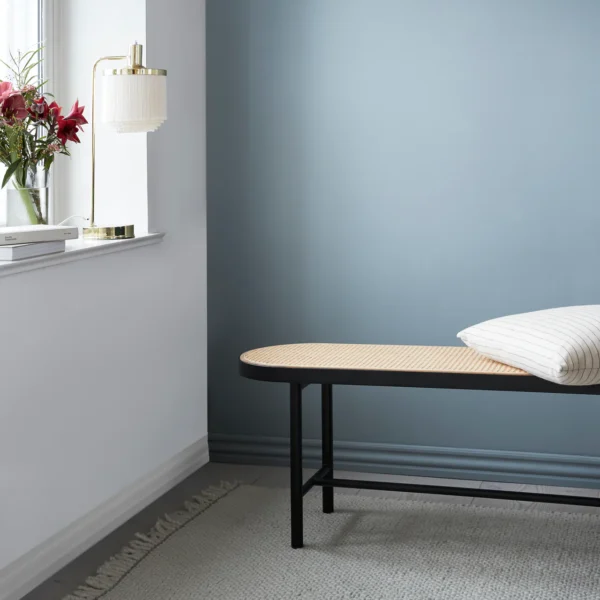 Tray rattan bench in front of a white and blue wall with a cushion on it