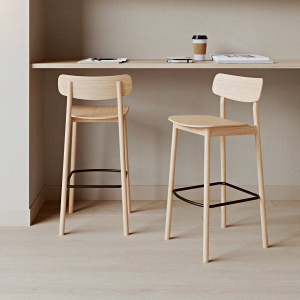 Yuri bar stool in natural oak wood, displayed in a minimalist modern interior with a wooden shelf filled with books and a coffee cup, enhancing the clean and functional aesthetic of the space