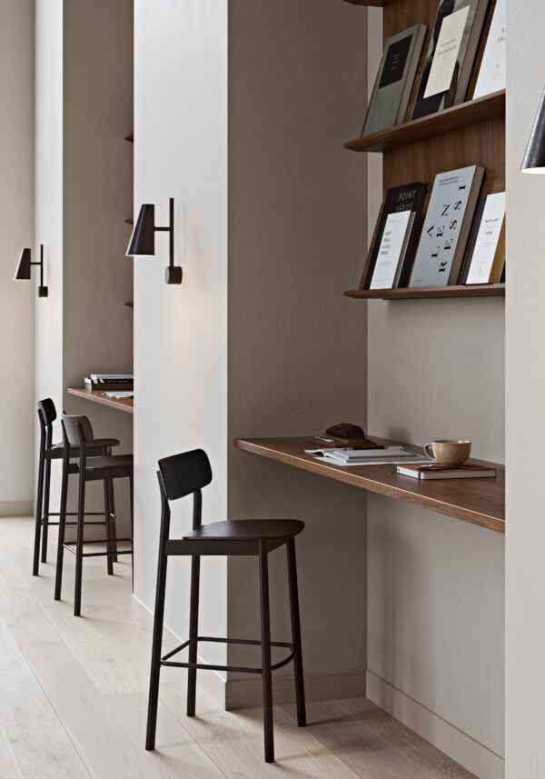 Yuri bar stools with black ash veneer seats and solid ash legs, aligned along a wooden bar table against a minimalist backdrop, ideal for contemporary office or home settings.