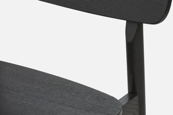 Close up of yuri dining chair, unupholstered in black oak showcasing meticulous joinery and beautiful oak grain