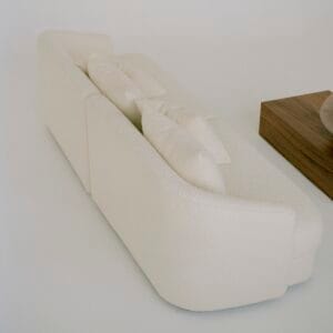 A rear view of the "Sophie" sofa in off-white boucle upholstery, showcasing its smooth, curved back design and plush cushions. A wooden coffee table is partially visible next to the sofa, maintaining the minimalist aesthetic.